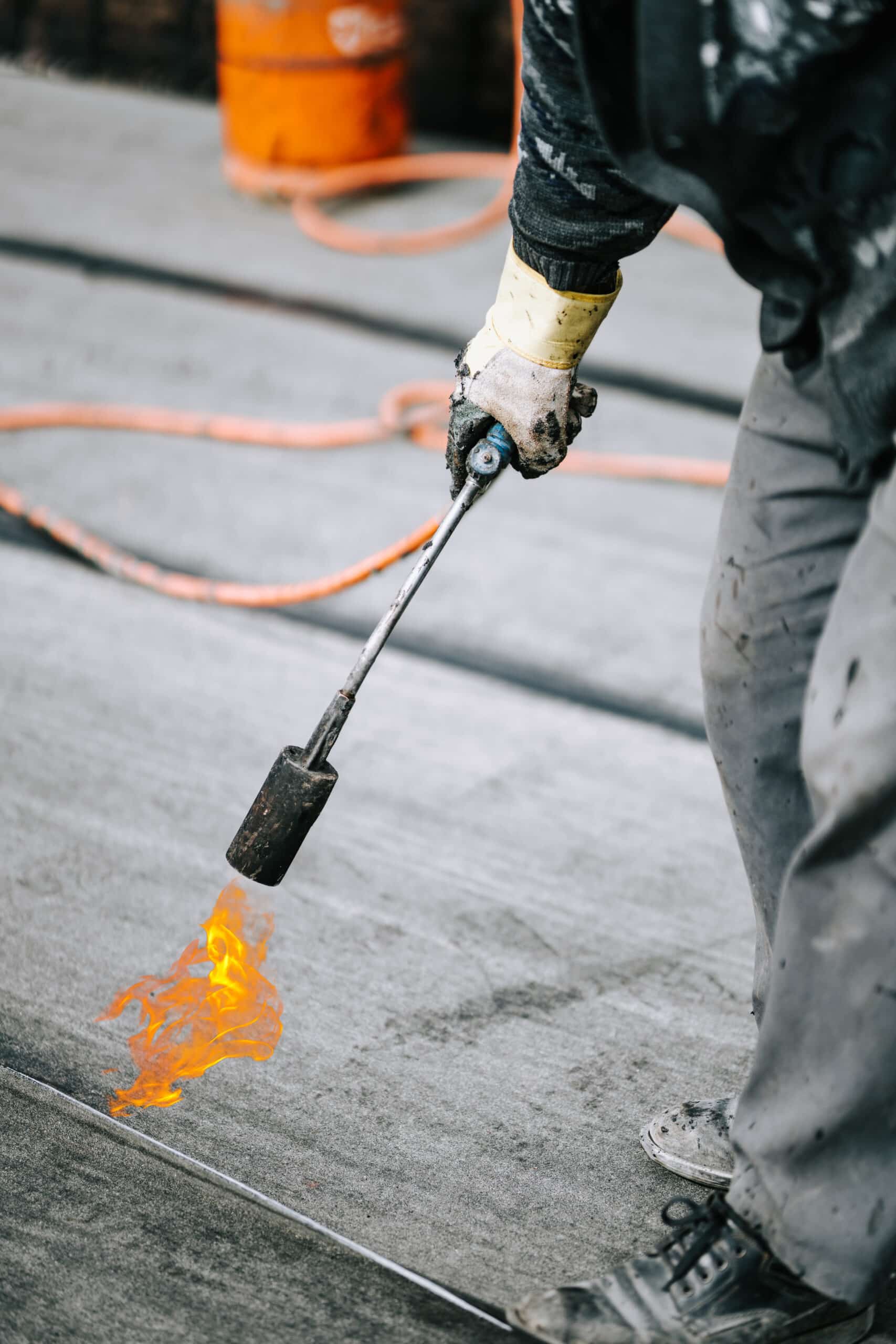 Preheating the edges of the roofing material. Repair work on the roof. Heating of the roofing material. Installation by heating and melting of bitumen rolls. waterproofing AdobeStock 490513010 scaled
